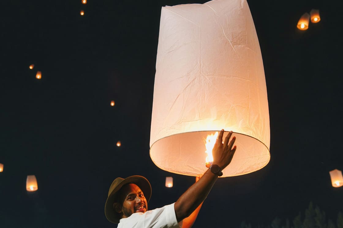 A smiling man releases a glowing paper lantern into a night sky already full of them