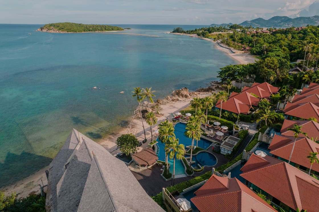 Aerial view of a Koh Samui beachfront resort — villas, pool and palms above a turquoise bay