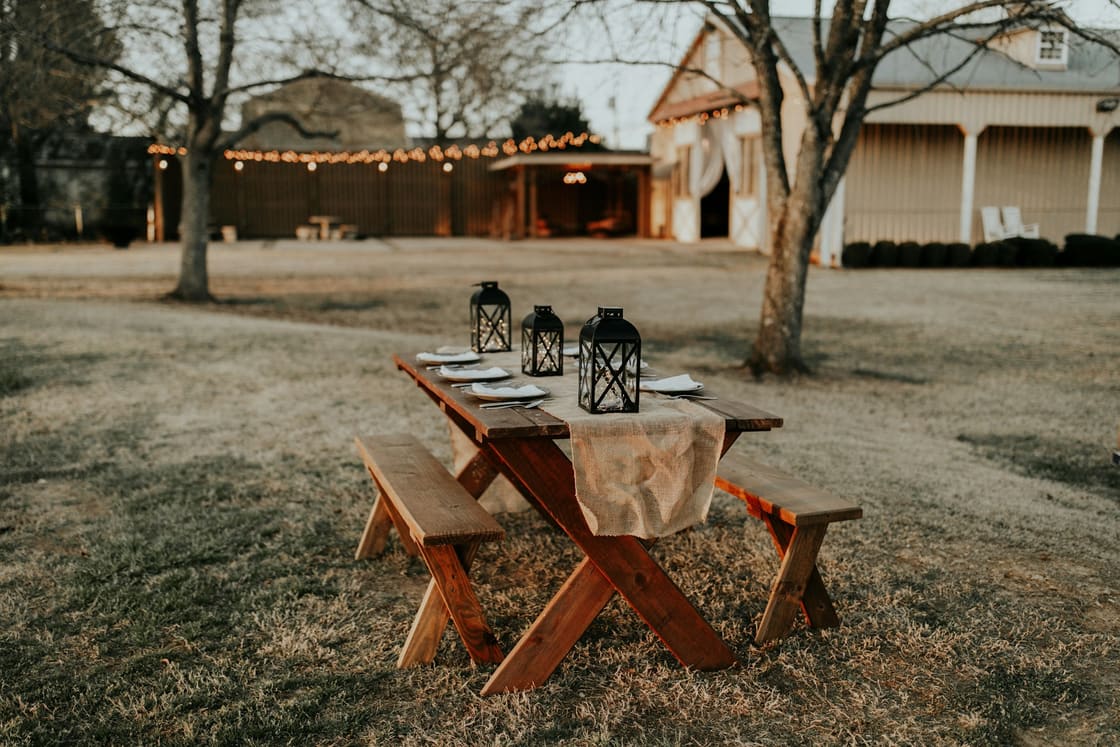 Rustic outdoor dinner table set with lanterns beneath string lights at dusk