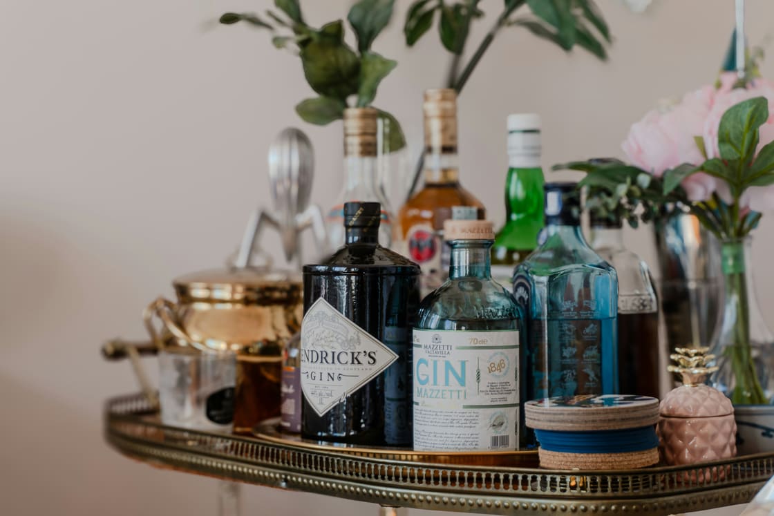 Brass bar cart topped with gin bottles, coasters and a vase of pink flowers
