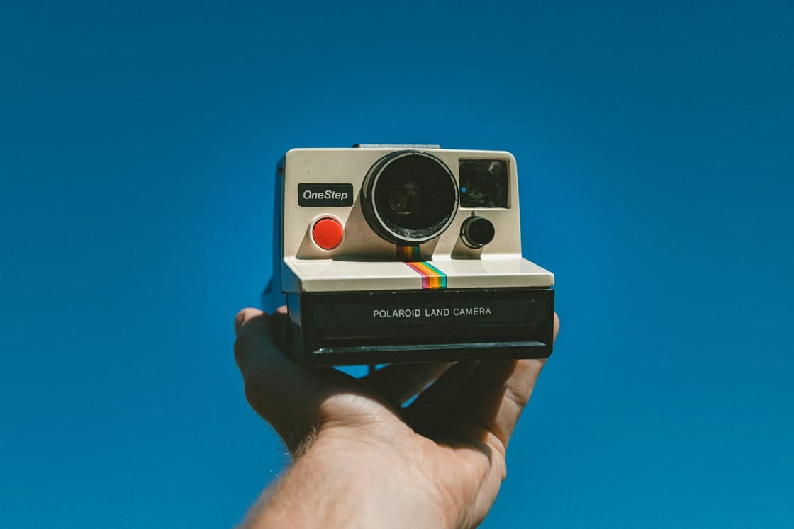 Hand holding a vintage instant camera against a bright blue sky