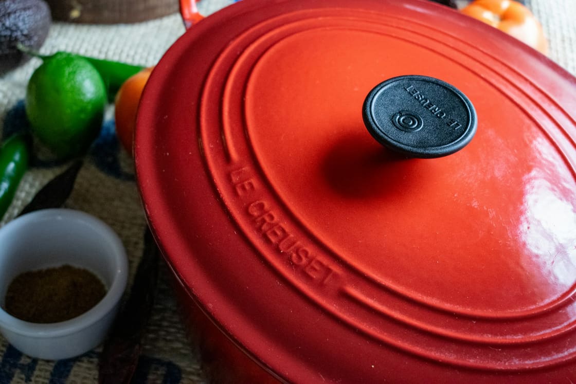 Red enamelled cast-iron pot on a table beside limes and spices