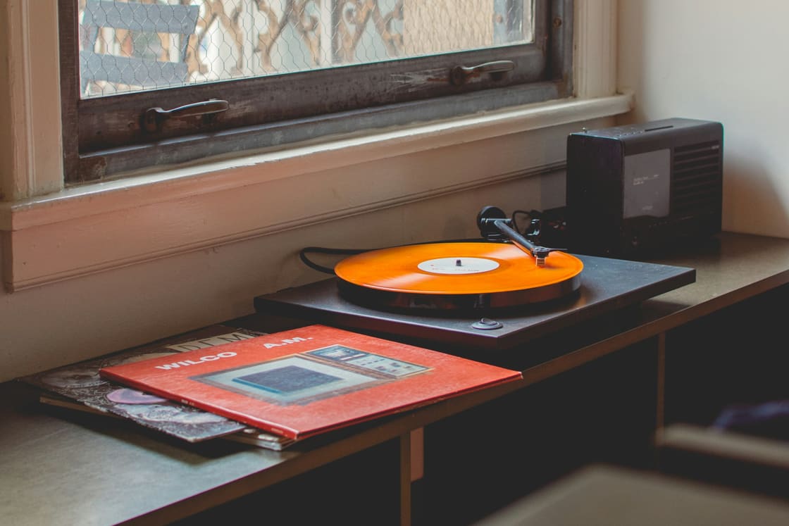 Turntable spinning an orange vinyl record on a sideboard by a window