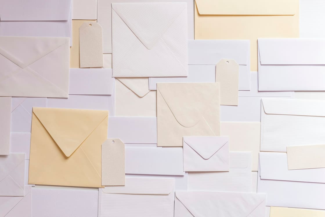 Cream and white envelopes and paper tags arranged in an overlapping flat lay